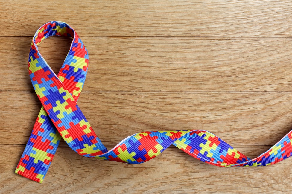 World Autism awareness and pride day with Puzzle pattern ribbon on wooden background